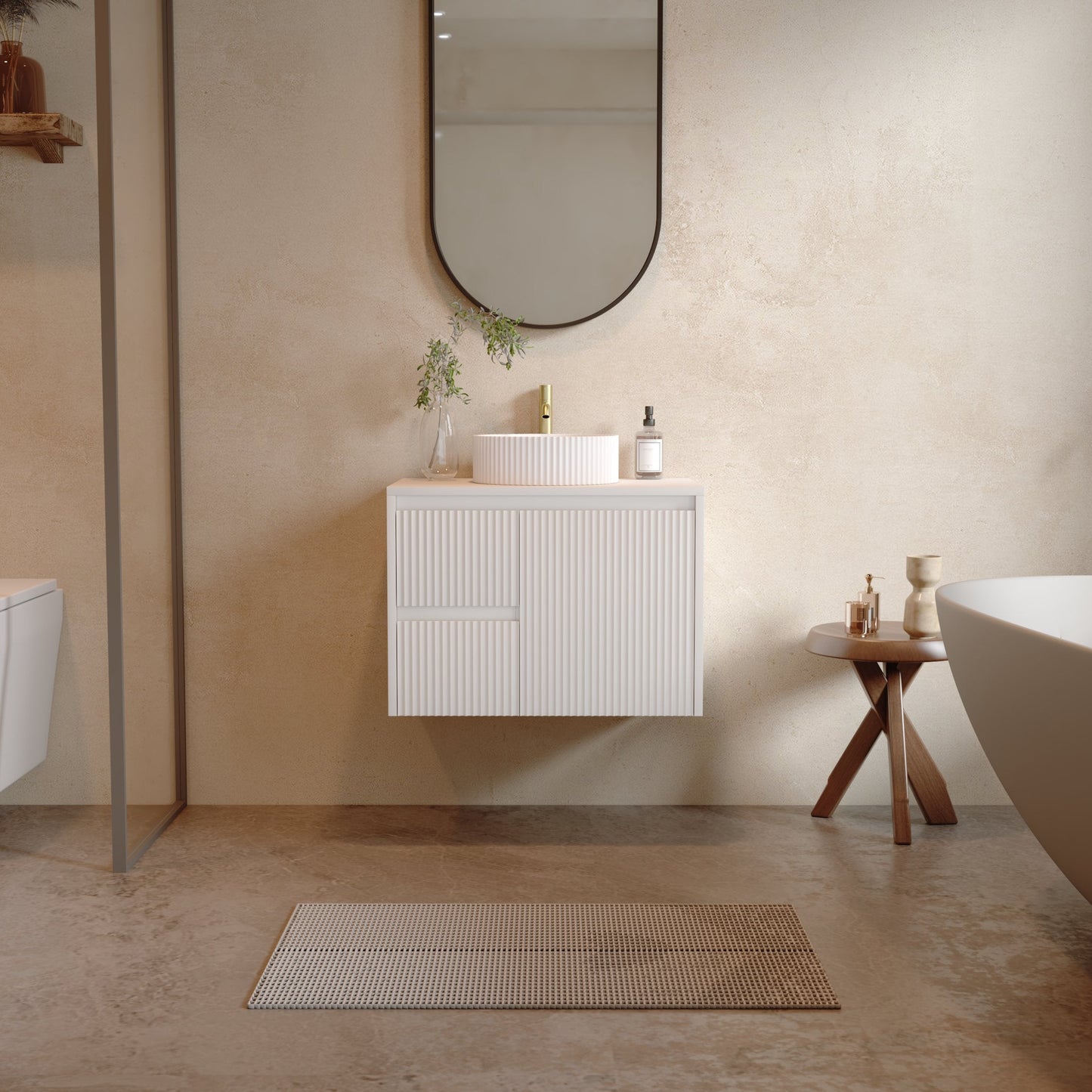 A modern bathroom scene featuring a white floating vanity cabinet with a white vessel sink, a round black-framed mirror, a small wooden side table, and a freestanding white bathtub. The room has textured beige plaster walls and a matching beige tiled floor.
