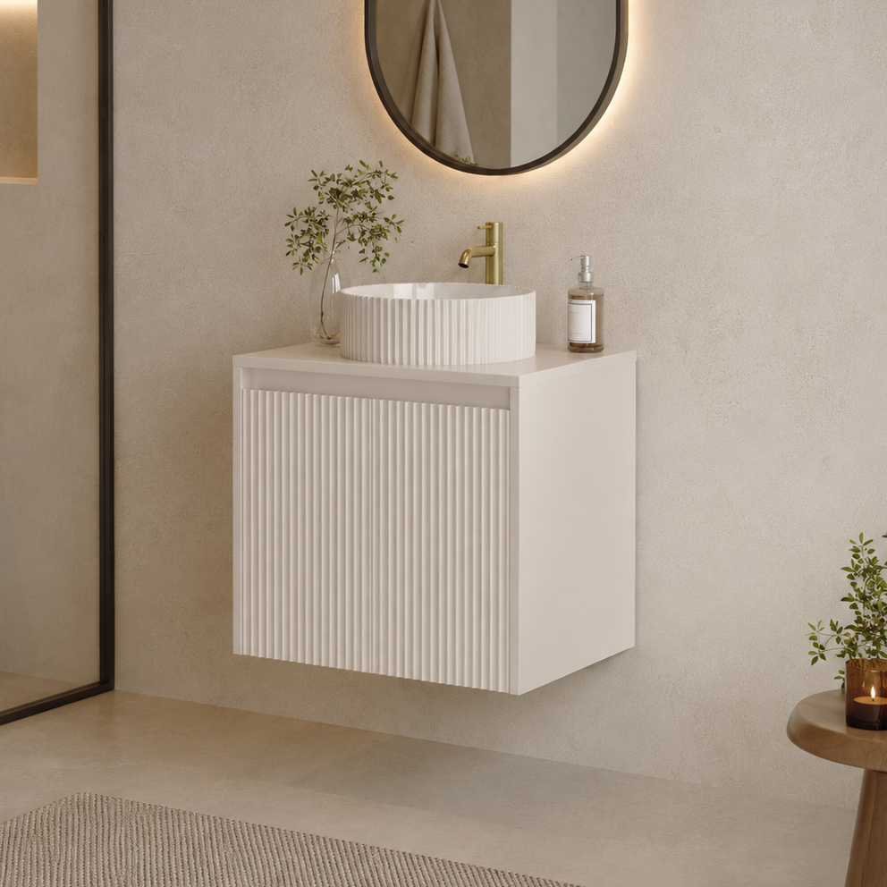 A modern floating bathroom vanity with a white ribbed cabinet, a matching white vessel sink, and a gold faucet, set against a textured beige wall with an oval mirror.