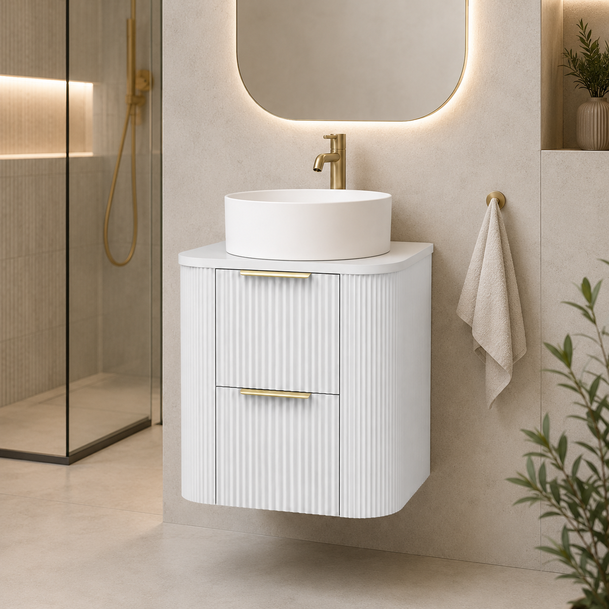 A modern floating bathroom vanity with a white round vessel sink and gold faucet, set against a beige tiled wall with a lit mirror and a hanging towel.